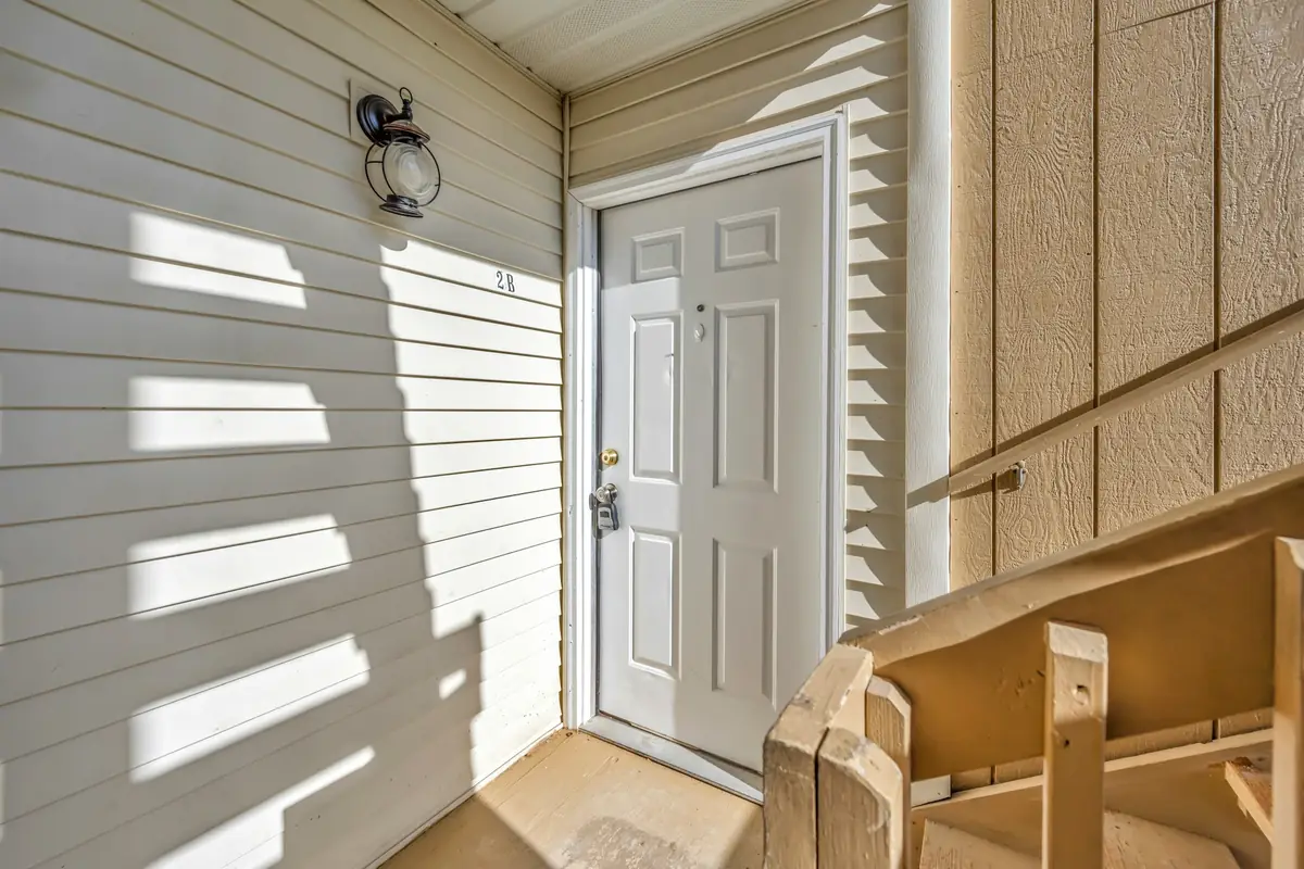 A white front door with a lever lock and a wall light, in morning sun